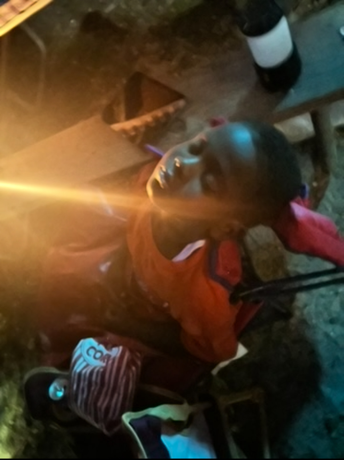 A close-up, low-light portrait of a child looking upwards, illuminated by a warm light source, likely the campfire.
