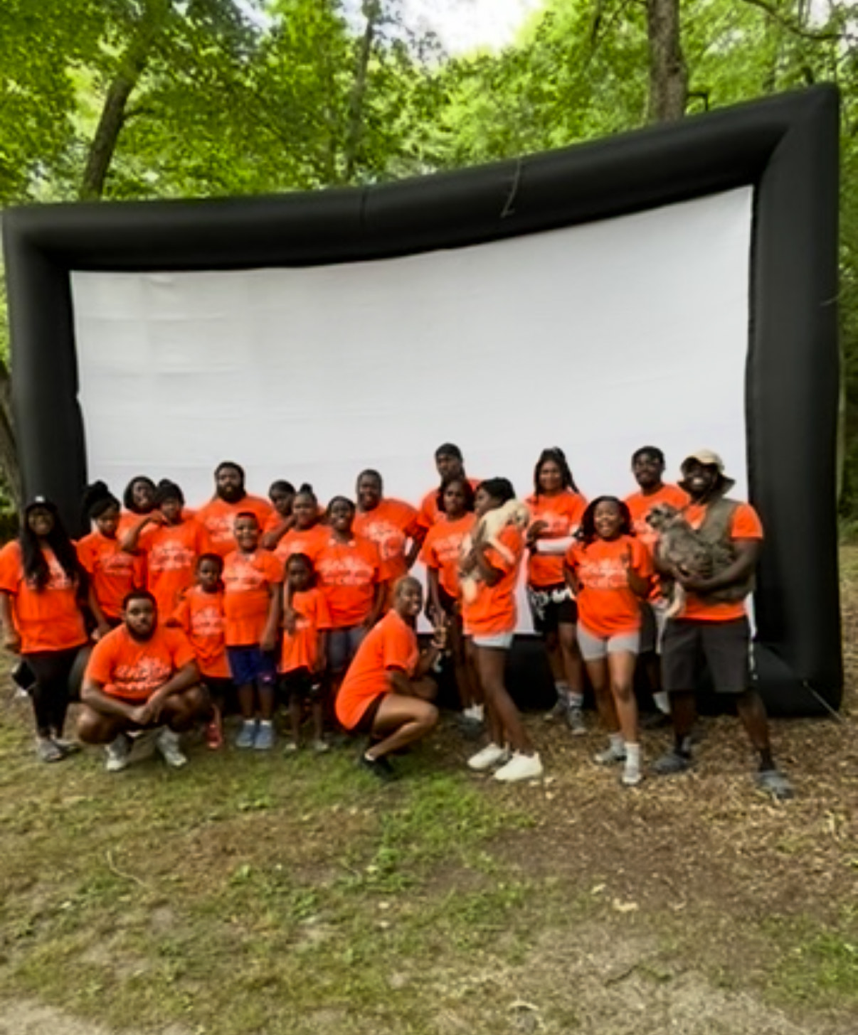 Large group of family and friends in orange shirts in front of an outdoor movie screen