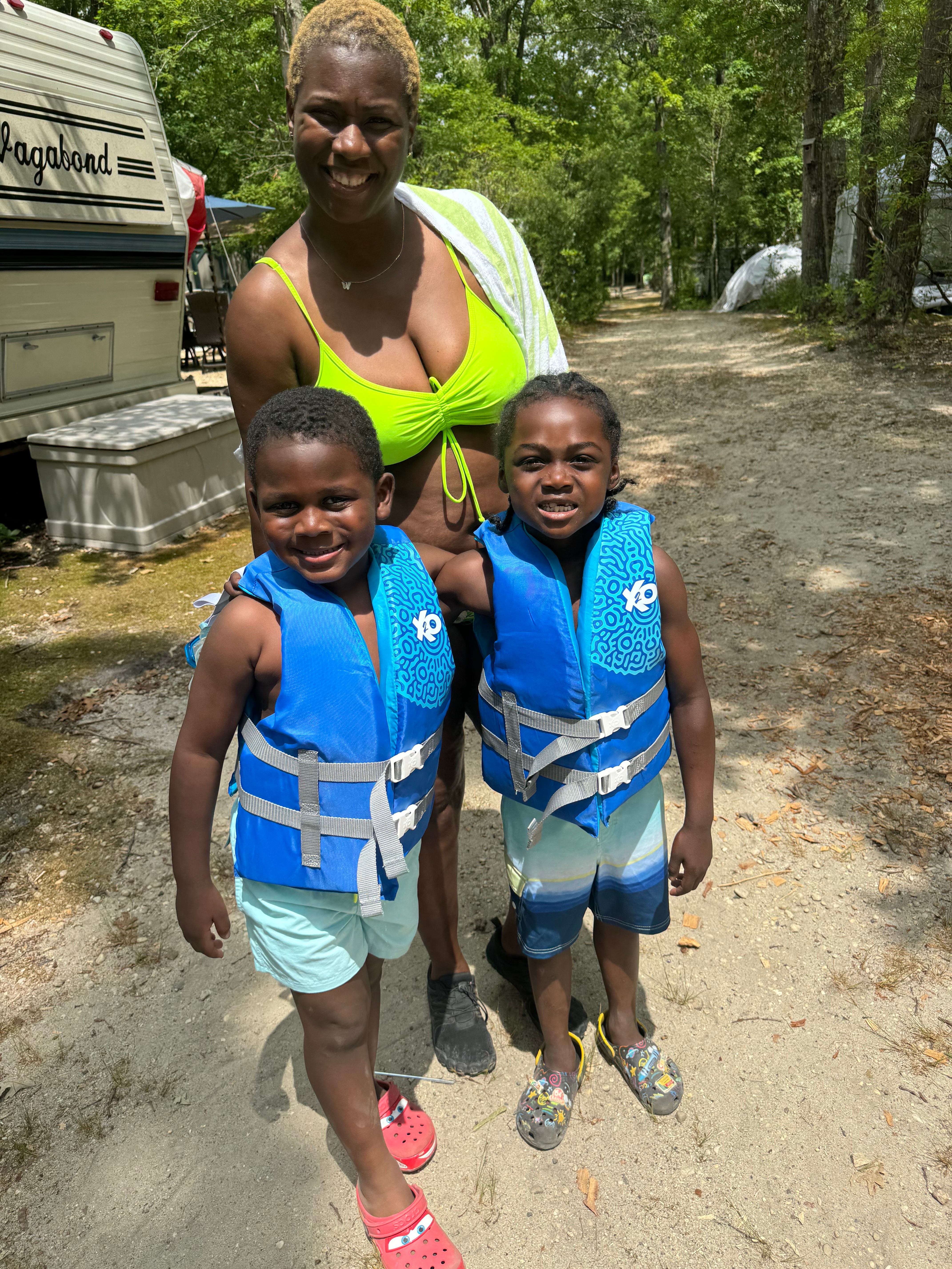 Woman in neon green swimsuit with two children in blue life vests.