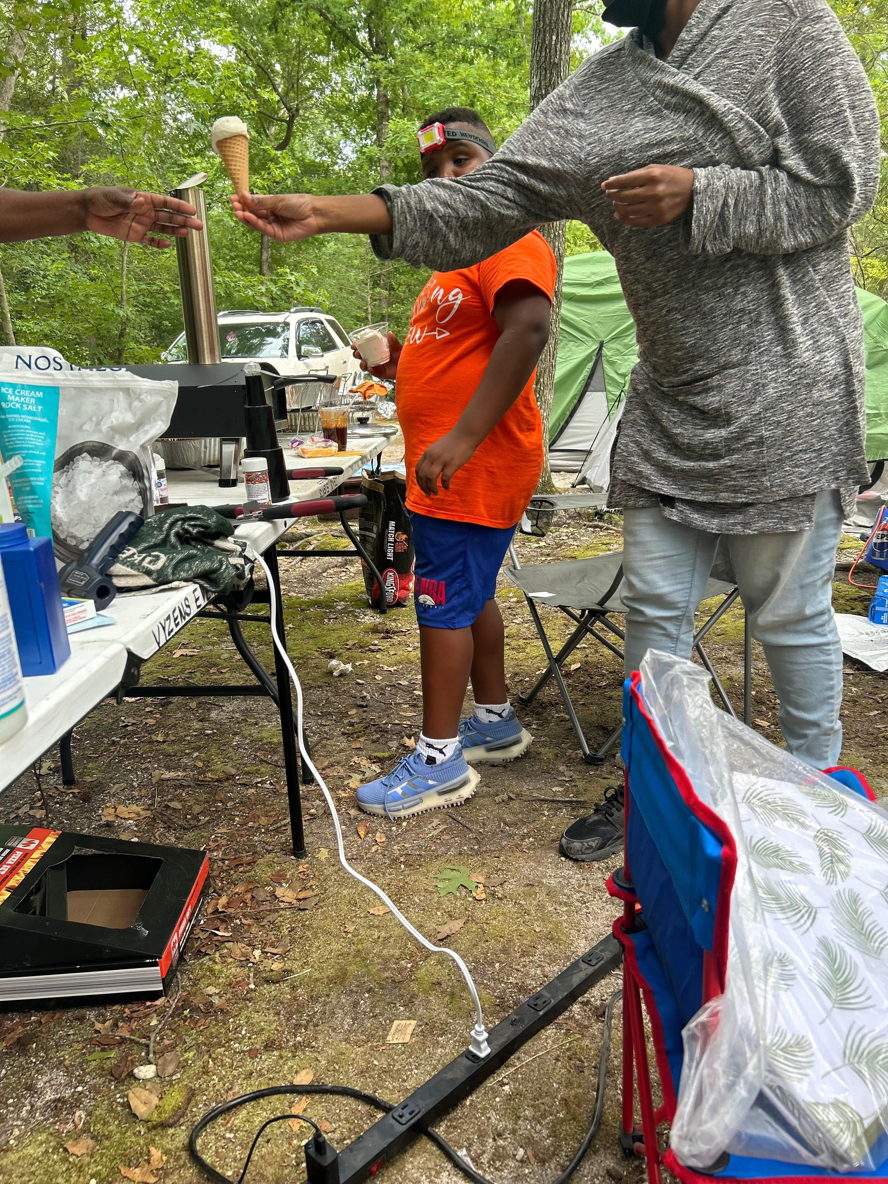 Person handing an ice cream cone to another person at a campsite.