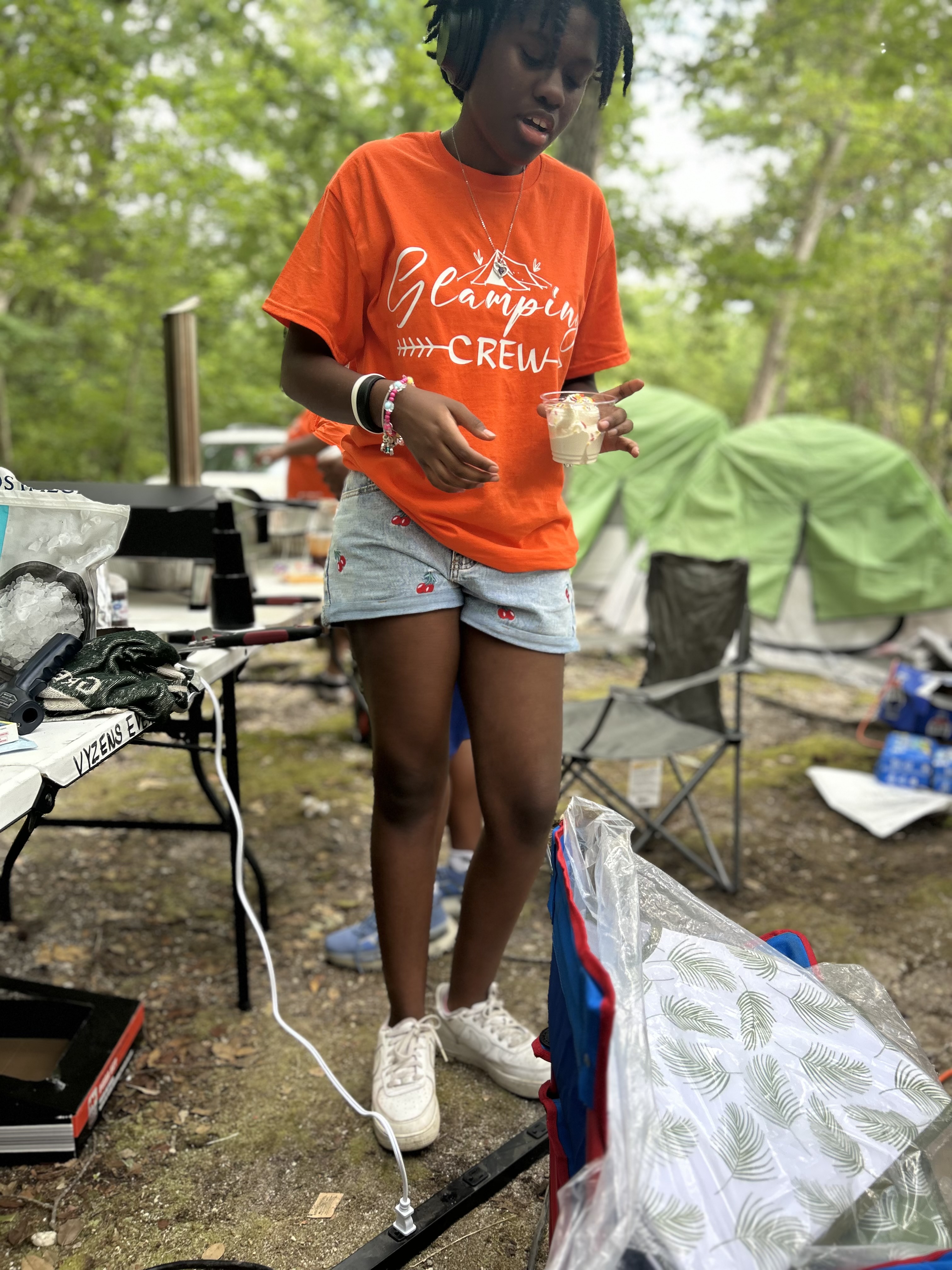 Young person in orange 'Glamping Crew' shirt holding ice cream cup.